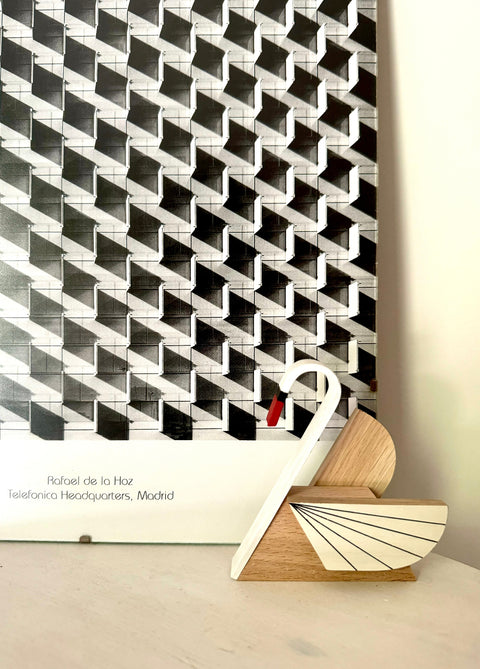 A black and white geometric patterned wall hanging or panel displayed indoors on a light surface, with a small wooden swan-shaped object in front and text at the bottom reading 'Rafael de la Hoz' and 'Telefonica Headquarters, Madrid'.