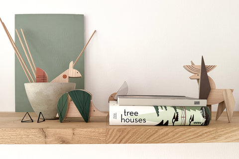 Wooden figurines and a book titled 'tree houses' on a shelf with a minimal background